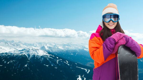 مفهوم زمستان اوقات فراغت ورزش و مردم - زن جوان شاد با عینک اسکی با اسنوبرد در پس زمینه کوه برفی