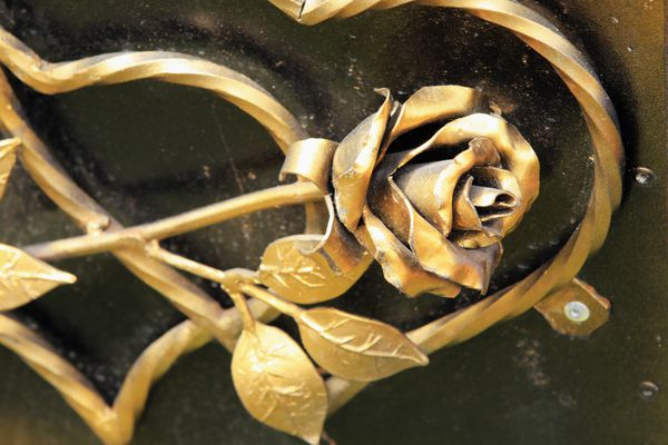 نمای نزدیک قلب و گل رز آهنی فرفورژه روی زمینه ای از فلز سیاه