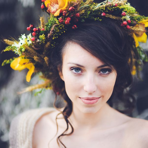 پرتره نزدیک از یک عروس دختر جوان زیبا با گل در موهایش با لباس سفید در پس زمینه ای از جنگل پاییزی جذاب به نظر می رسد و برگ ها در حال ژست گرفتن و لبخند زدن