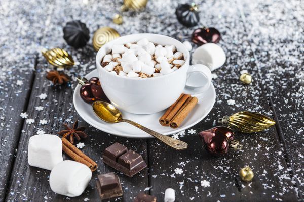 فنجان شکلات با گل ختمی و تزئینات کریسمس روی میز برفی