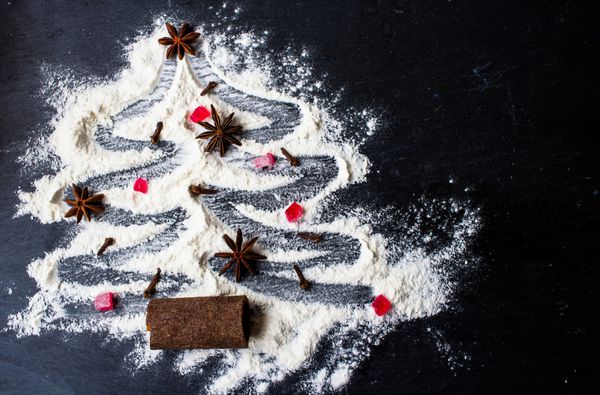 درخت کریسمس ساخته شده از آرد روی زمینه سیاه با ستاره های انیسون و چوب دارچین