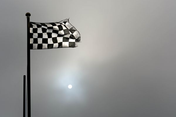 پرچم شطرنجی یا شطرنجی مسابقات اتومبیل رانی در سپیده دم مه آلود با آفتاب آبکی که در میان مه می سوزد