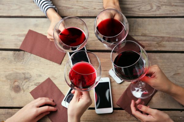 چهار دست با تلفن‌های هوشمند که عینک‌هایی با رنگ قرمز در دست دارند روی پس‌زمینه میز چوبی