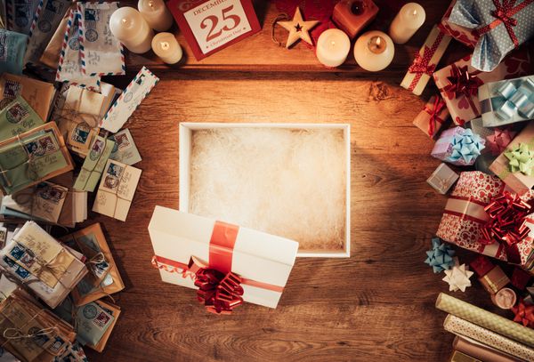 جعبه خالی هدیه کریسمس را روی یک رومیزی چوبی که با حروف و هدایا احاطه شده است نمای بالا باز کنید