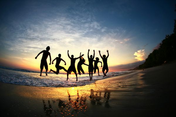 گروهی از دوستان که از شادی در ساحل استوایی در غروب آفتاب می پرند