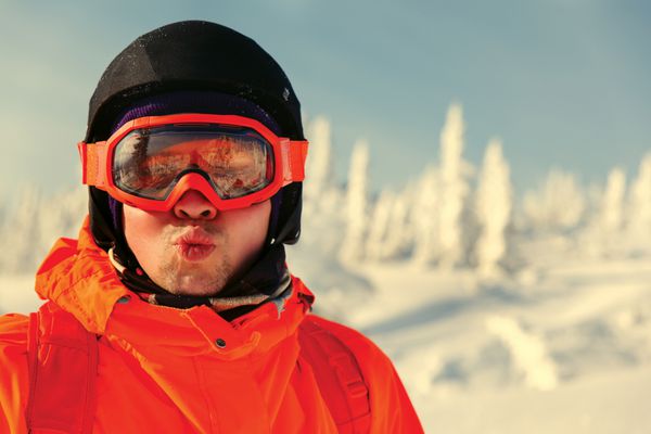 پرتره اسنوبرد سوار در استراحتگاه زمستانی با ماسک عینک آفتابی در پیست اسکی در کوهستان