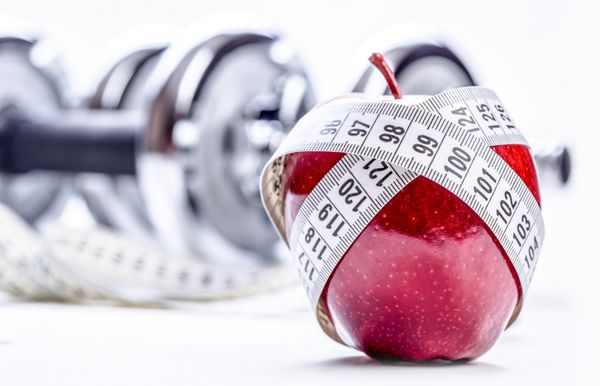 سیب قرمز تازه متر نواری و در پس زمینه دمبل های تناسب اندام رژیم غذایی سبک زندگی سالم و ورزش استودیو اس