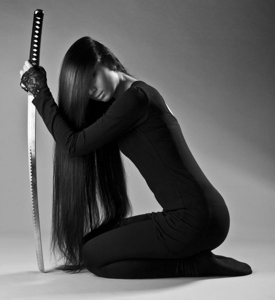 دختر نینجا مو بلند یا زن قاتل زانو زده و شمشیر کاتانا را در دست گرفته است
