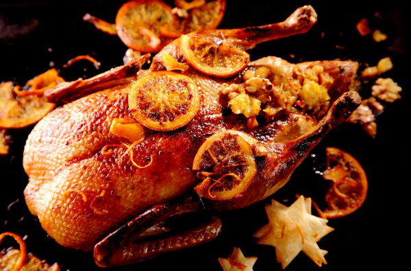 اردک کریسمس کبابی پر لعاب تزیین شده با برش های پرتقال ترشی شده و با ستاره های تزئینی شیرینی سرو شده نمای با زاویه بالا برای یک شام سنتی و خوشمزه تعطیلات