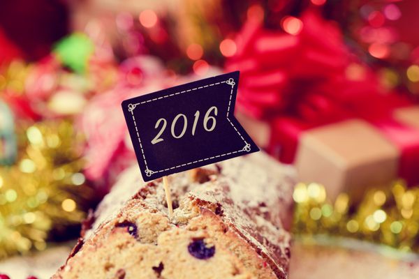 نمای نزدیک از یک کیک میوه با پرچم سیاه با شماره 2016 به عنوان سال جدید روی یک میز پر از هدایا و زیور آلات کریسمس