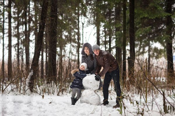 خانواده شاد آدم برفی را در پارک زمستانی مجسمه می کنند