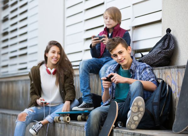 سه نوجوان اسپانیایی مثبت با گوشی های هوشمند در روز پاییزی در فضای باز