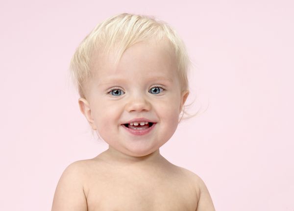 پرتره کودک قفقازی کودک کوچولو با چشم‌های نزدیک دندان‌های پوست با لبخند شاد روی پس‌زمینه صورتی استودیو به دوربین نگاه می‌کند 1 سال