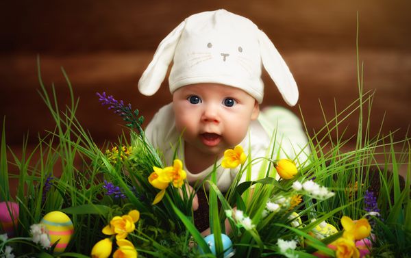 کودک شادی با لباس خرگوش اسم حیوان دست اموز عید پاک که روی چمن روی چمن با گل دراز کشیده است