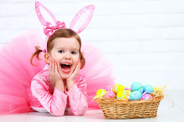 دختر بچه شاد با لباس خرگوش اسم حیوان دست اموز عید پاک با گوش و یک سبد تخم مرغ