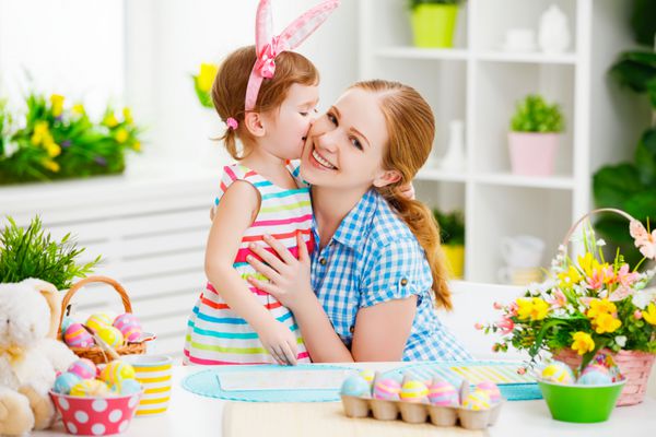 خانواده شاد عید پاک را جشن می گیرند مادر و دختر در حال بوسیدن در خانه با تزئین تخم مرغ و گل های چند رنگ