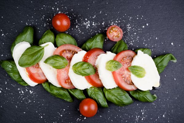 سالاد کاپرز ایتالیایی تازه با موزارلا و گوجه فرنگی در بشقاب تیره