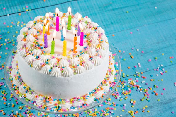 کیک تولد با آبپاش های رنگارنگ و شمع روی پس زمینه آبی