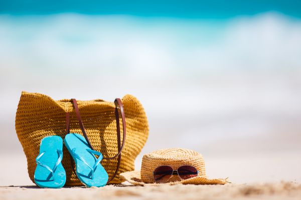 کلاه حصیری کیف عینک آفتابی و دمپایی در یک ساحل استوایی