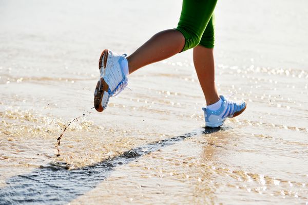 پاهای زن جوان در حال دویدن در ساحل هنگام طلوع آفتاب