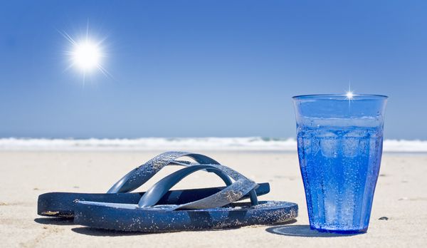 لیوان آب گازدار و صندل در ساحل با آسمان و خورشید