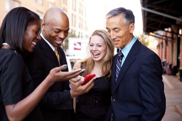 گروهی از افراد تجاری که به تلفن همراه نگاه می کنند و می خندند