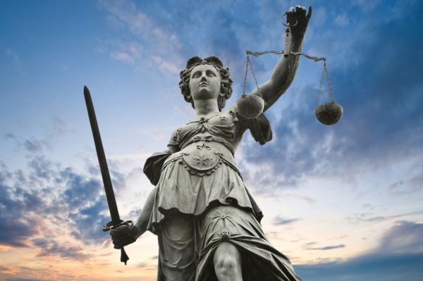 مجسمه عدالت با شمشیر و مقیاس آسمان ابری در پس زمینه