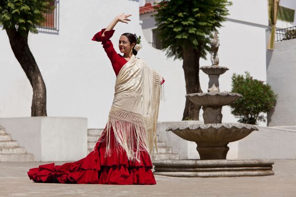 رقص زن سنتی فلامنکو اسپانیایی با لباس قرمز و شال کرم در میدان شهر با فواره سنگی