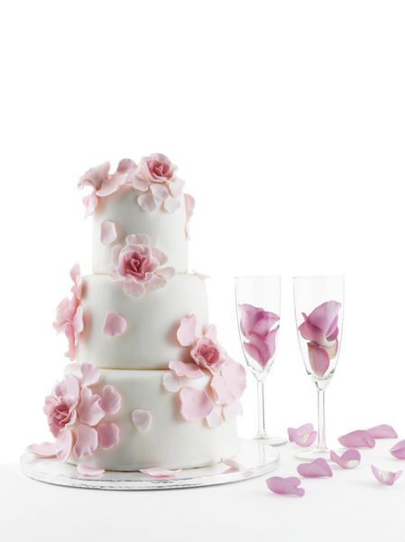 کیک عروسی مجلل با گل و دو لیوان فلوت شامپاین با گلبرگ های رز پس زمینه استودیو سفید جدا شده با کپی اسپ