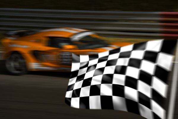 ماشین مسابقه‌ای نارنجی که از پرچم شطرنجی با تاری حرکت عبور می‌کند