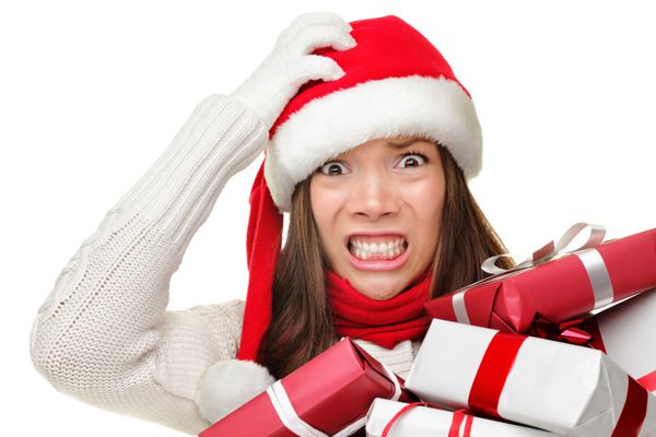 استرس کریسمس - زن شلوغی که کلاه بابا نوئل بر سر دارد و برای خرید کریسمس استرس دارد ممکن است هدایای کریسمس را در آغوش خود نگه دارد تصویر خنده دار از مدل زن قفقازی آسیایی جدا شده در پس زمینه سفید