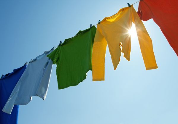 لباس‌های رنگارنگ برای خشک شدن روی خط لباس‌شویی آویزان شده و خورشید در آسمان آبی می‌درخشد