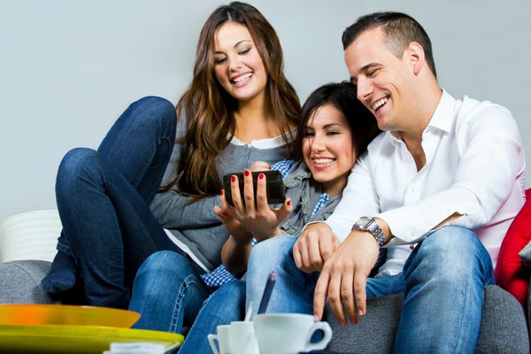 دو دختر و پسری که با موبایل روی کاناپه خانه خوش می گذرانند