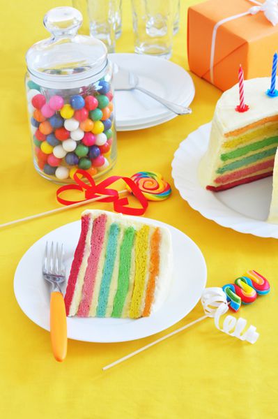 تکه کیک رنگین کمانی روی میز تولد
