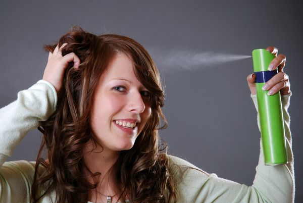 زن جوان موهای خود را با اسپری مو حالت می دهد