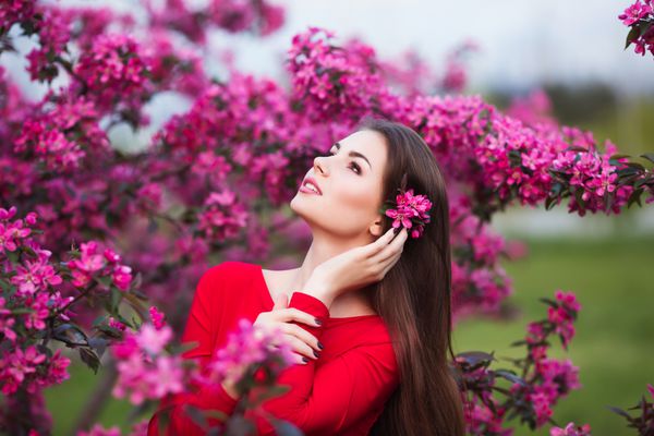 زن جوان زیبای شاد در پارک شکوفه با درختان و گل ها
