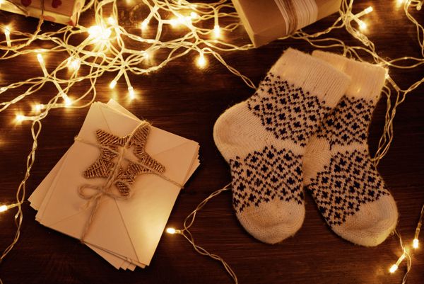 جوراب های پشمی گرم با هدایای کریسمس و تزئینات روی زمینه چوبی نزدیک