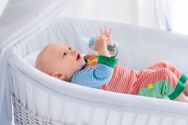 نوزاد کوچک با شیشه شیر در تخت سفید