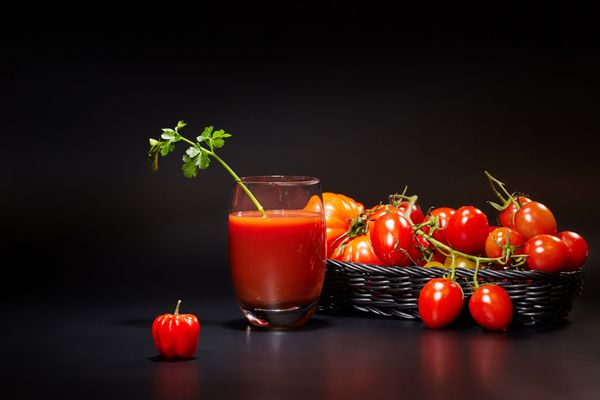لیوان آب گوجه فرنگی با سبزیجات در پس زمینه سیاه