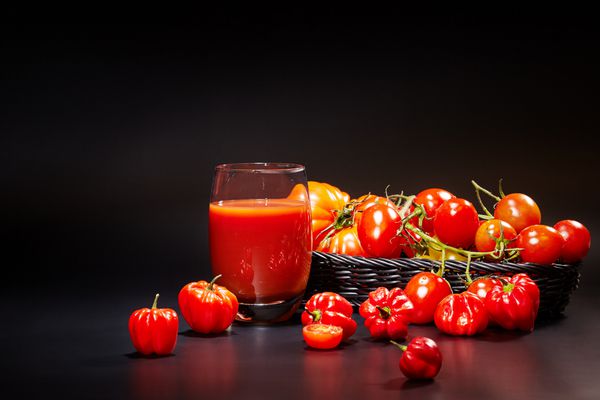 لیوان آب گوجه فرنگی با سبزیجات در پس زمینه سیاه