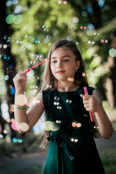 دختر بچه قفقازی در حال دمیدن حباب های صابون در فضای باز