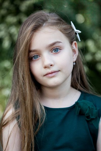 پری بهاری پرتره دختر کوچک زیبا با موهای قهوه ای و چشمان آبی که در فضای باز روی پس زمینه طبیعی ایستاده است