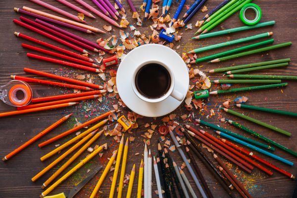 مداد رنگی و یک فنجان قهوه در زمینه چوبی