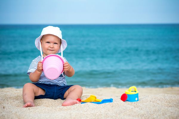 پسر زیبا در ساحل با اسباب بازی و شن