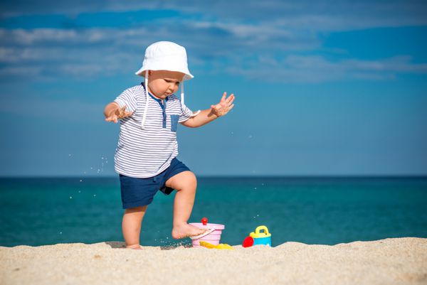 پسر کوچولوی دوست داشتنی که در ساحل ایستاده است