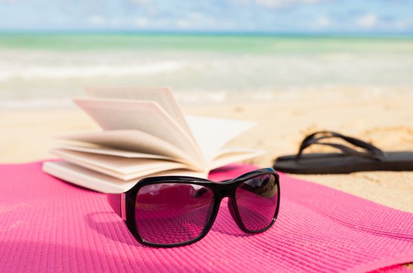 کلاه کتاب و عینک آفتابی در ساحل استوایی