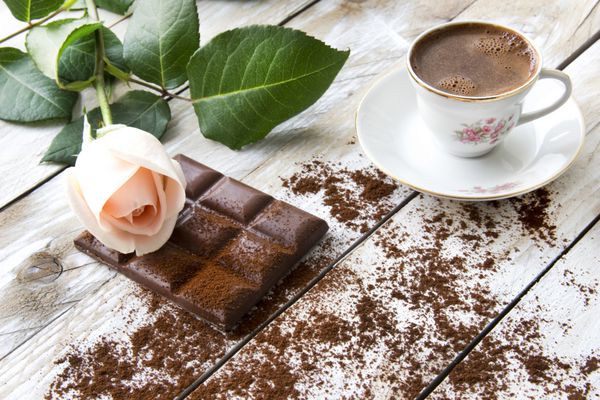 قهوه ترک با گل رز هلویی رنگ و تکه های شکلات روی میز چوبی