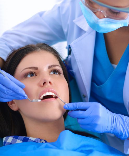 زن دندانپزشکی که روی دندان های بیمارش کار می کند