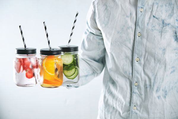 مردی ناشناخته شیشه هایی با نوشیدنی های تازه سرد را برای خنک شدن در تابستان ارائه می دهد نوشیدنی های سالم ساخته شده از توت فرنگی پرتقال خیار نعناع یخ و آب گازدار در شیشه های روستایی