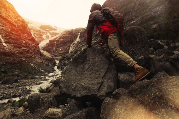 مسافر جوان شجاع با یک کوله پشتی در حال بالا رفتن از یک در پس زمینه یک یخچال طبیعی